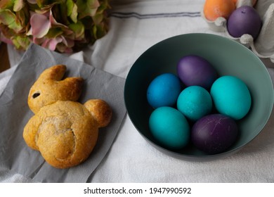 Easter Eggs In A Bowl In Blue, Turquoise, Purple, And Orange, And Brioche Shaped Like An Easter Bunny.