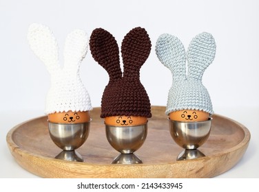 Easter Eggs In Crocheted Hats With Bunny Ears In An Egg Stand On A Wooden Tray. Soft Focus. Home Easter Decoration Concept.