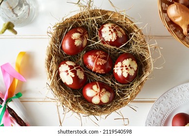 Easter eggs dyed with onion peels with a pattern of fresh herbs in a wicker basket, with pomlazka - Czech symbol of spring, top view