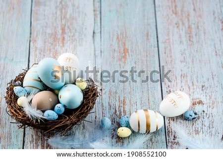 Easter eggs, feathers in a nest on a blue wooden background. The minimal concept. Top view. Card with a copy of the place for the text.