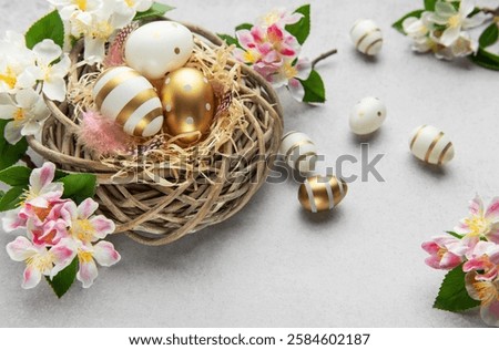 Easter eggs with gold decorations lying in a wicker nest with spring flowers and feathers