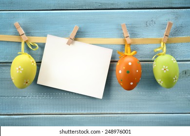 Easter Eggs Hanging On Wood Background With Blank Card.