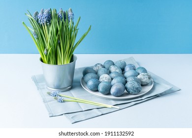 Easter eggs and Muscari in decorative bucket on light blue background.
