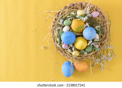 Easter eggs in nest on yellow background. Top view with copy space.