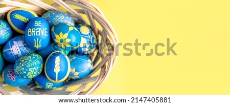Easter eggs in straw basket, painted with Ukrainian national colors, blue and yellow, and depicting Ukrainian national symbols: spikelet of wheat, sunflower, trident, viburnum