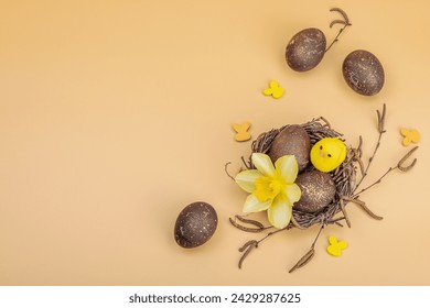 Easter eggs, wooden bunnies and bird's nest with chicken and narcissus flower. Festive concept, greeting card, flat lay, pastel apricot background, top view - Powered by Shutterstock