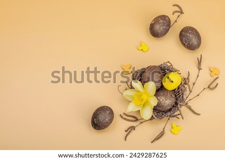Easter eggs, wooden bunnies and bird's nest with chicken and narcissus flower. Festive concept, greeting card, flat lay, pastel apricot background, top view