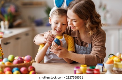 Easter Family traditions. Loving young mother teaching happy little kid soon to dye and decorate eggs with paints for Easter holidays while sitting together at kitchen table, selective focus - Shutterstock ID 2127588521