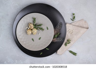 Easter  festive table setting with  gray plate, quail eggs leaf sprigs of eucalyptus. On a gray concrete background.