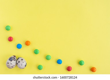 Easter flat lay with quail eggs and tiny candy on yellow background. Top view, copy space