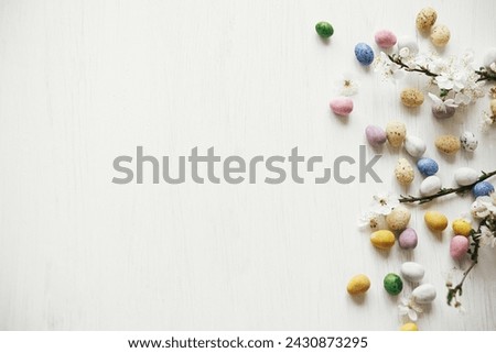 Easter flat lay. Stylish easter chocolate eggs and cherry blossom on rustic white table. Happy Easter! Easter border with space for text. Modern candy colorful eggs and spring flowers