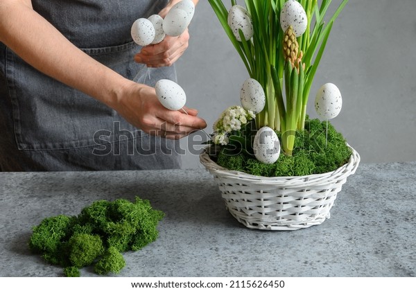 Easter\
floral DIY composition for table centerpiece with white eggs, moss\
and bunny. Close up. Woman make spring\
decor.