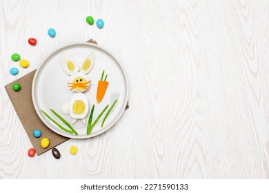 Easter funny creative healthy breakfast lunch food idea for kids children.Bunny rabbit made from boiled eggs,peeled carrots, greens on plate white wood table background.Top view Flat lay, copy space.
