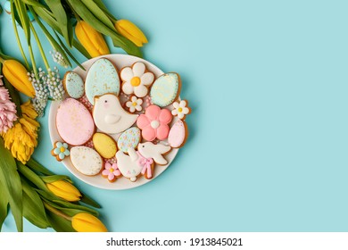 Easter gingerbread with icing on plate, seasonal flowers on blue, festive Easter background web banner, copy space. Easter card with traditional treats. Sweet Easter concept, greeting card