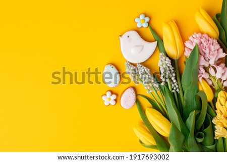 Easter gingerbread with icing, seasonal flowers on yellow table, festive Easter background web banner, copy space. Easter card with traditional treats. Sweet Easter concept, greeting card