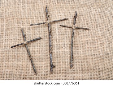 Easter or Good Friday image of three handmade crosses made out of twigs or sticks tied with twine on a rough textured background made of burlap