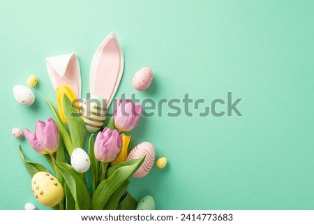 Easter happiness in photo! Overhead perspective of a bouquet adorned with tulips and vibrant eggs, complemented by quirky bunny ears. Displayed on mint-green background, ready for personalized message