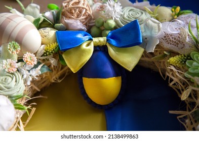 Easter holiday composition - a decorative wreath and an egg with a satin bow, painted in yellow and blue colors of the Ukrainian flag. Easter concept. Stand with Ukraine