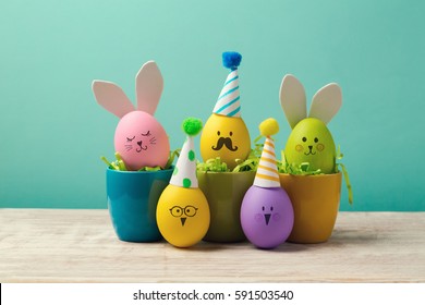 Easter holiday concept with cute handmade eggs in coffee cups, bunny, chicks and party hats