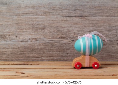 Easter holiday concept with egg on toy car over wooden background