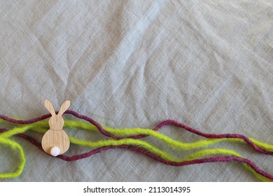 Easter holiday light blue textile background with wooden rabbit shape and violet and green wool yarn.