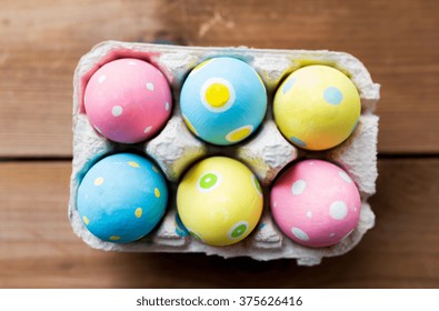 easter, holidays, tradition and object concept - close up of colored easter eggs in egg box or carton wooden surface