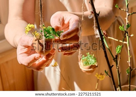 Easter home decoration. Woman's hands hanging egg shell with small wildflowers on spring twigs as easter decoration.Easter floral arrangement.