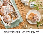 Easter Hot cross buns. Traditional Easter treats cross buns with raisins, butter, chocolate candy eggs with blossoming cherry or apple flowers on rustic light wooden backgrounds. Easter holiday meal.
