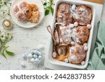 Easter Hot cross buns. Traditional Easter treats cross buns with raisins, butter, chocolate candy eggs with blossoming cherry or apple flowers on rustic light wooden backgrounds. Easter holiday meal.