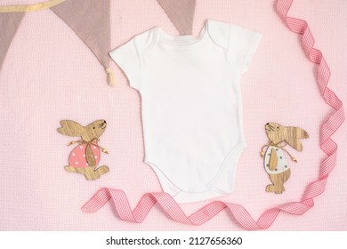 Easter mockup baby bodysuit onesie with bunny and easter eggs on pink cover background. Flatlay, top view, copyspace.