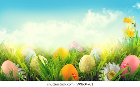 Easter nature spring scene background. Beautiful colorful eggs and flowers in spring grass meadow over blue sky with sun. Invitation card border design
