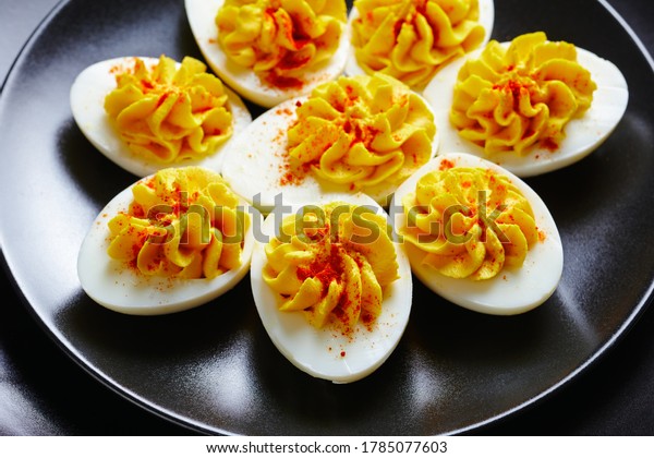 Easter party\
snack deviled eggs of smashed egg yolks, dijon mustard, mayonnaise,\
apple cider vinegar sprinkled with smoked paprika on a black plate\
with golden cutlery,\
close-up
