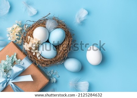 Easter pastel background with eggs, a nest and a gift on a blue background. The concept of a Happy Easter. Top view, copy space.
