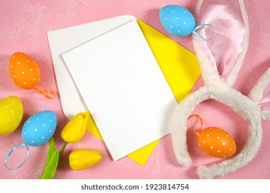 Easter product mockup with bunny ears and easter eggs on pink background flatlay. White greeting card and yellow envelope mock up with negative copy space for your text or design here.