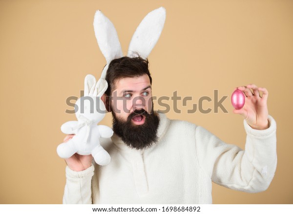 Easter rabbit. Man wearing rabbit suit. Funny\
bunny man soft ears. Easter activities concept. Weirdo concept.\
Celebrate Easter. Guy bearded hipster weird bunny with long white\
ears beige background.