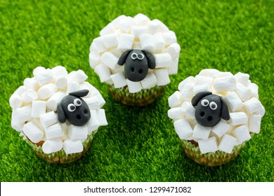 Easter Sheep Cupcakes On Green Grass Background, Homemade Cup Cakes Shaped Funny Sheeps With Marshmallow And Black Fondant Icing Faces, Creative Treats For Kids On Easter Holiday