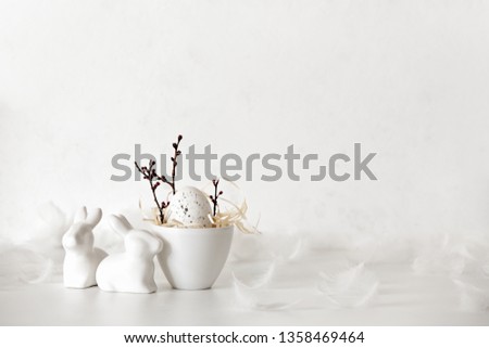 Easter simple decorative composition idea, front view on easter egg in a bowl and ceramic rabbits, blank space for greeting text 