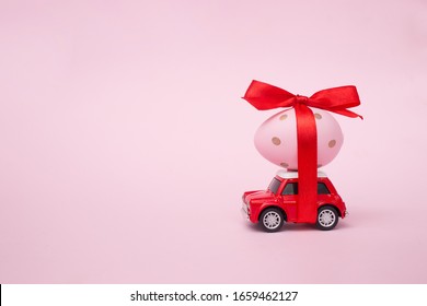 Easter Spring Holiday Concept With Egg On Red Toy Car On Pink Pastel Background. Copy Space