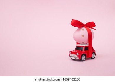 Easter Spring Holiday Concept With Egg On Red Toy Car On Pink Pastel Background. Copy Space