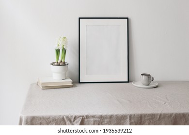 Easter Spring Still Life. Blank Black Picture Frame Mockup On Linen Table Cloth. Old Books On Cup Of Coffee And Hite Hyacinth In Flower Pot. Home Office Concept. Scandinavian Interior Design.