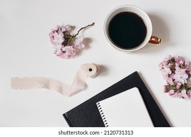 Easter, Spring Still Life. Blank Diary Mockup. Cup Of Coffee, Blooming Pink Japanese Cherry Tree Branches Isolated On White Table Background. Home Office. Breakfast, Break Concept. Flat Lay, Top View.