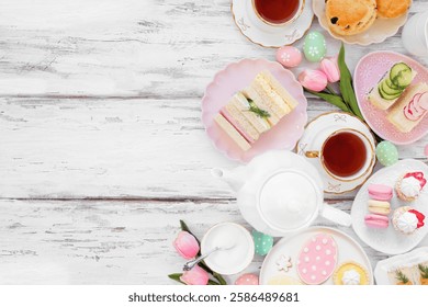 Easter or spring tea side border against a white wood background. Selection of finger sandwiches, scones and sweet desserts. Top down view. Copy space.