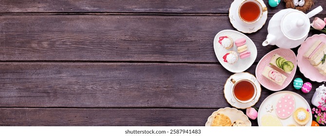 Easter or spring tea side border against a dark wood banner background. Selection of finger sandwiches, scones and sweet desserts. Top view. Copy space.