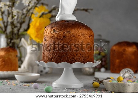 Easter sweet bread or Easter cake - Paska with white sugar glaze and colored sprinkles on top on a concrete background. Person decorates cake with hand. Copy space