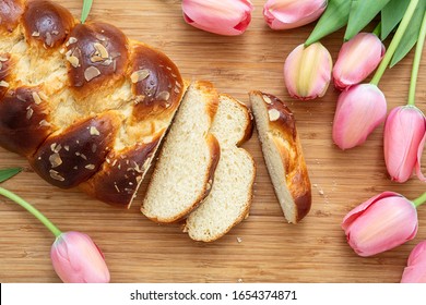 Easter sweet bread, tsoureki cozonac sliced on wood table background, pink tulips decoration, top view. Easter time, springtime