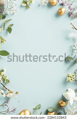 Easter table decorations. Happy Easter concept with golden easter eggs, feathers and spring flowers on blue background. Flat lay top view copy space