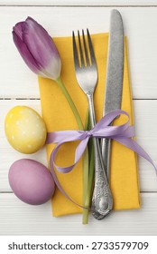 Easter table setting. Beautiful silverware with tulip and painted eggs on white wooden background, top view