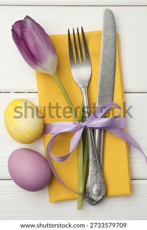 Easter table setting. Beautiful silverware with tulip and painted eggs on white wooden background, top view