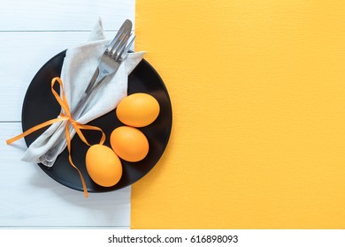 Easter table setting with cutlery. Rustic orange table cloth on white wood background. Holidays background with copy space.