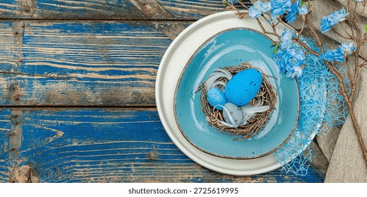 Easter table setting with eggs, bird's nest and blooming branch. Traditional festive symbols, greeting card, flat lay. Old wooden boards background, banner format